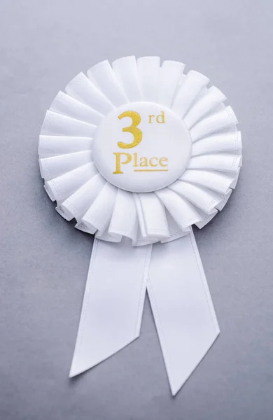 Third placed white ribbon rosette on grey — Stock Photo, Image