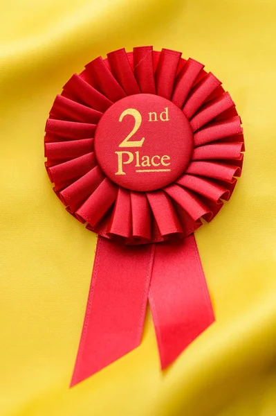 Red 2nd Place winners rosette on gold fabric — Stock Photo, Image