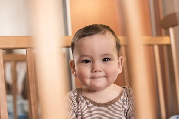 Милый улыбающийся малыш смотрит через кроватку — стоковое фото