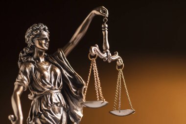 Kahverengi arka planda, gözleri bağlı bronz Adalet Heykeli. 