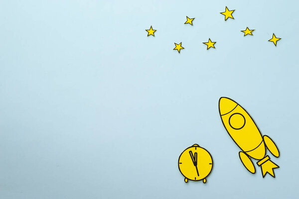 Yellow carton rocket with clock and stars on blue