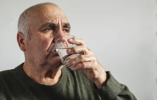 Elderly man taking medication with water in a close up portrait