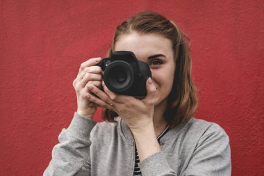 Dışarıda duran genç bir kadın renkli kırmızı bir duvarın fotoğrafını çekiyor.