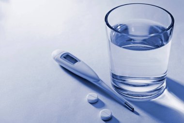 Tabletler, klinik termometre ve beyaz bir zemin üzerinde su bardağı bir hastalık veya hastalık için kavramsal tedavi ve doz ilaç