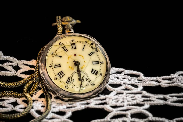 artistic low key image of antique broken pocket watch on black velvet fabric and white lace