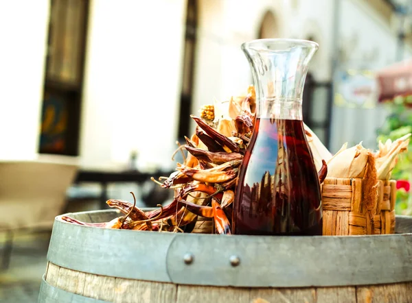 a carafe of red wine next to hot peppers on a barrel
