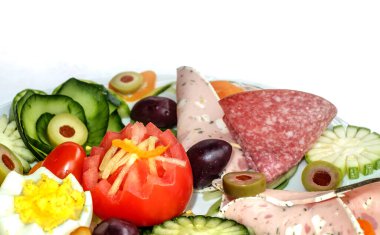 Kahvaltı tabağında salatalık, domates, jambon, salam, yeşil ve mor zeytin, sarı peynir, haşlanmış yumurta ve kırmızı dolma biber.