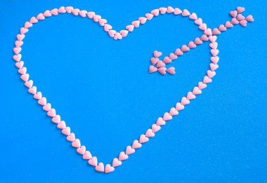 Kalp şekli, mavi arka plandaki küçük pembe şekerlerden yapılmış okla delinmiş.