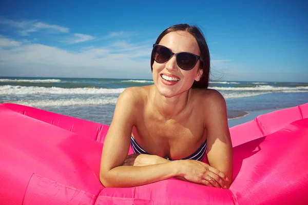 Положительная женщина лежит на животе на розовой надувной лодке и p — стоковое фото