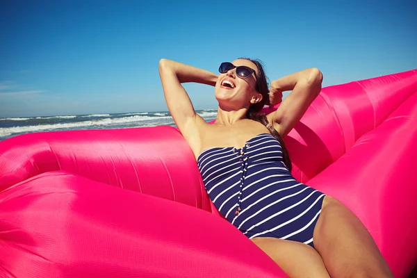 A woman grinning from ear to ear on the rose-colored inflatable — Stockfoto