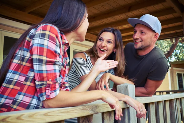 Drei glückliche Freunde, die auf der Terrasse stehen und plaudern — Stockfoto