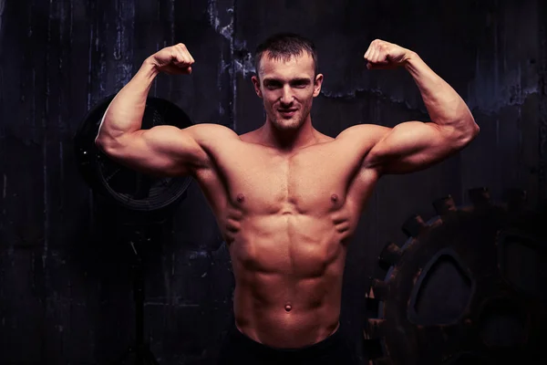 Handsome young bodybuilder posing shirtless in dim light of the — Stock Photo, Image