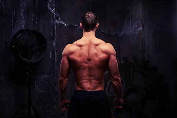 Visão traseira do corpo masculino perfeitamente treinado contra a parede escura áspera — Fotografia de Stock