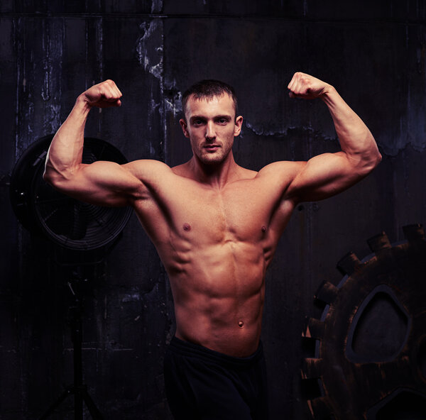 Young bodybuilder with toned trained body against rough grey wal