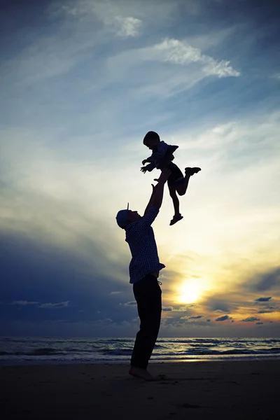 Silhouette of the dad tossing up a child at the sunset while sta — Stock Photo, Image