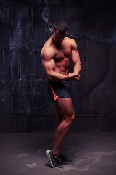 Musculoso hombre de pecho desnudo en pantalones cortos deportivos en el estudio contra la oscuridad — Foto de Stock