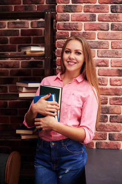 Menina caucasiana em jeans e blusa rosa segurando livros — Fotografia de Stock