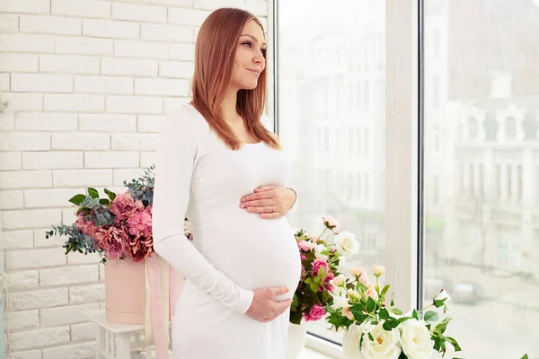 Liebevolle liebevolle Mutter, die einen schwangeren Bauch hält, während sie schaut — Stockfoto