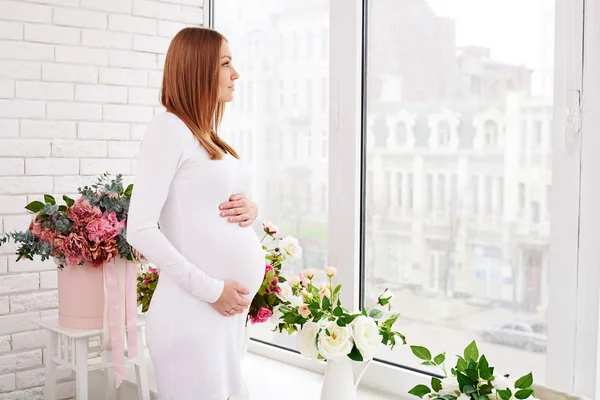 Беременная молодая женщина задумчиво смотрит в окно — стоковое фото