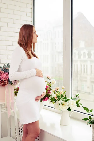 Сентиментальная беременная женщина смотрит в окно, держа в руках b — стоковое фото