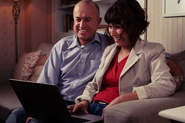 Ett leende par som sitter på soffan inomhus titta i laptop — Stockfoto