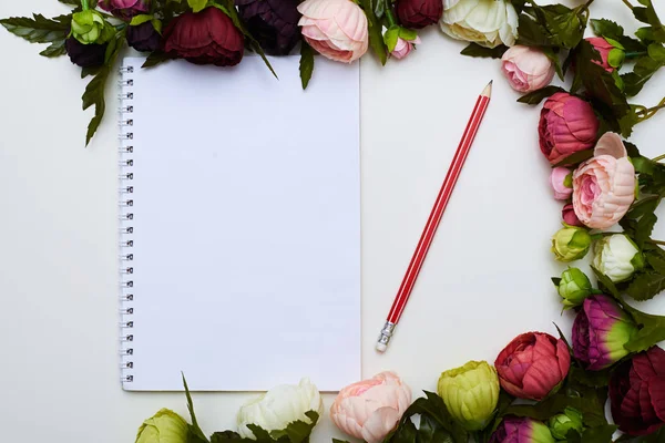 Jotter en rood potlood omcirkeld door kleurrijke bloemen — Stockfoto