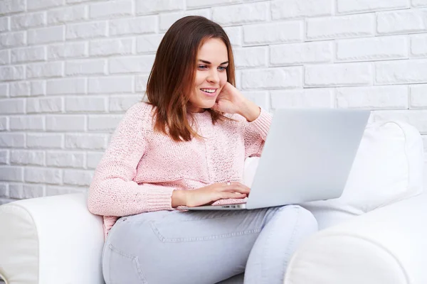 En ung söt dam med ett upptäckande leende tittar på hennes laptop — Stockfoto