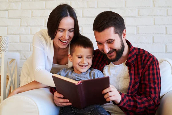 Familia riendo juntos mientras leen un libro divertido — Foto de Stock