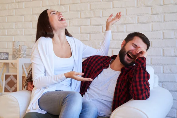 Pareja humorística riendo de una broma, sentado en la sala de estar en —  Fotos de Stock