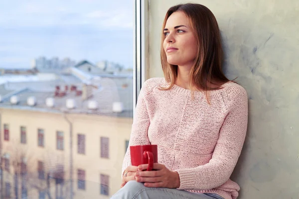 Вдохновлённая молодая девушка держит чашку кофе и смотрит сквозь — стоковое фото
