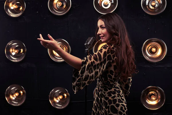 Side view of tempting woman beckoning with hand singing in a mic — Stock Photo, Image