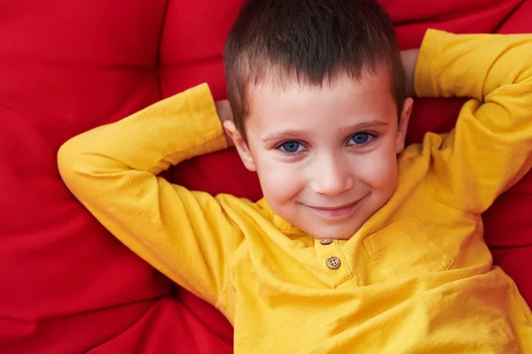 Small boy with cornflower blue eyes holding hands behind head wh — Stock Photo, Image