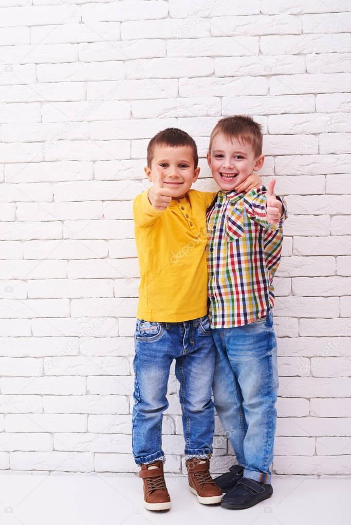 Two excited boys hugging each other and showing thumbs up 