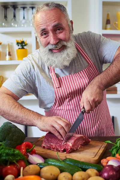 Kocken skärande klump av kött som tittar på den kamera står på den — Stockfoto