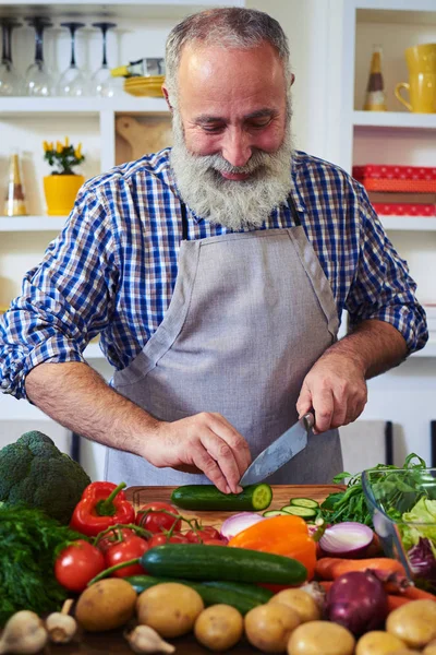Nahaufnahme eines älteren Mannes, der eine Schürze trägt und Gemüse hackt — Stockfoto