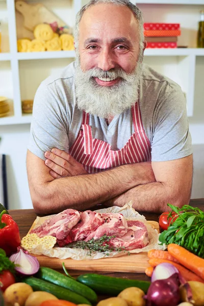 Close-up of cheerful chef in apron leaning on the table — Stock Photo, Image