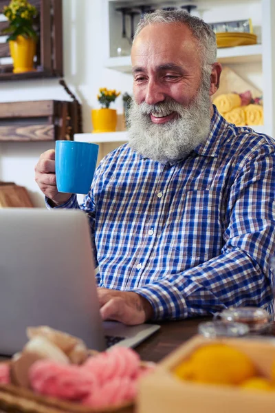 Очарованный человек пьет чай и пользуется ноутбуком, проводя время — стоковое фото