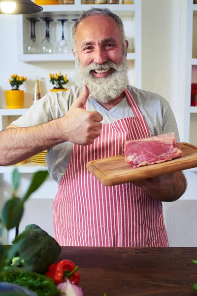 Excited mature man showing thumb up while holding a cutting boar — Stock Photo, Image