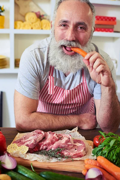 Funny man biting carrot while cooking at home — Stock Photo, Image