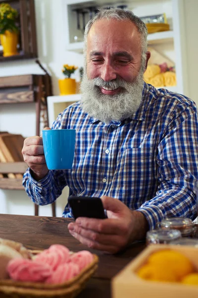 Homme utilisant un smartphone et tenant un thé au café assis à l'onglet — Photo