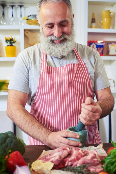 Mid shot of a gray bearded man grinding spices on cutting board