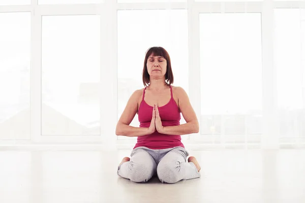 Тонка жінка роздумує в спортзалі, сидячи на килимку для йоги — стокове фото
