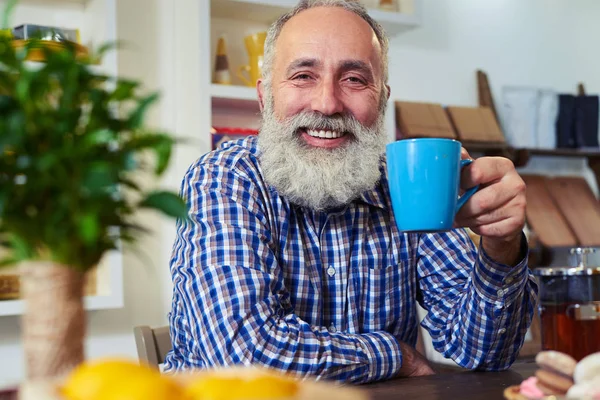 Smiley senior man holding cup of tea in hands while leaning on t — Stock Photo, Image