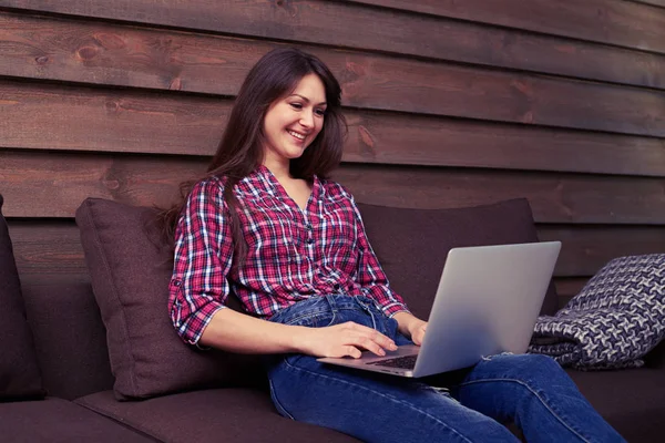 Smiley γυναίκα που κάθεται στον καναπέ στο σπίτι πληκτρολόγηση στον υπολογιστή και — Φωτογραφία Αρχείου