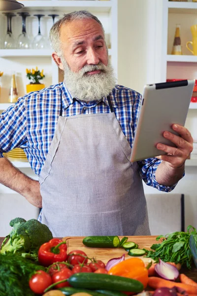Hombre reflexivo de pie en la cocina en busca de receta con —  Fotos de Stock