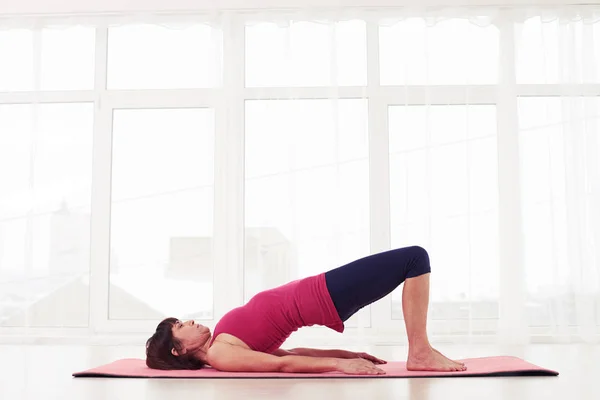 Жінка робить гімнастику позу мосту на рожевому килимку для йоги — стокове фото