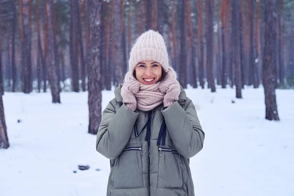 Cheerful young woman standing in a snowy forest holding a knitte — Stock Photo, Image