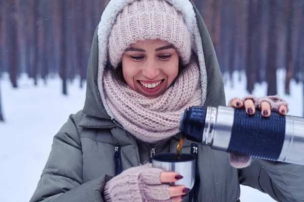 Feminino derramando chá de garrafa térmica para a xícara em uma floresta nevada — Fotografia de Stock