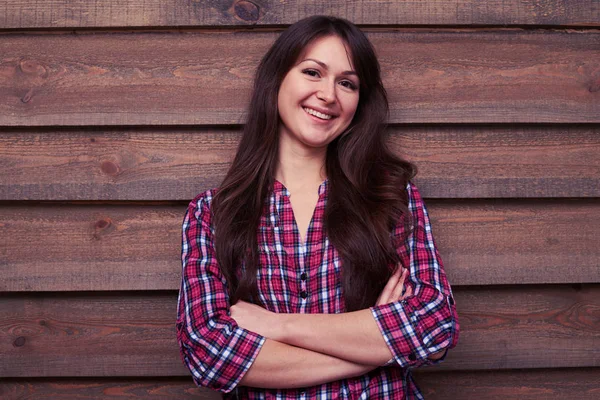 Long-haired brunette posing at the camera against wooden backgro — Stock Photo, Image