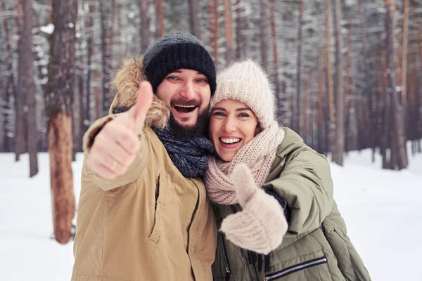 Smiling couple snowing thumbs up gesture and hugging on a cold w